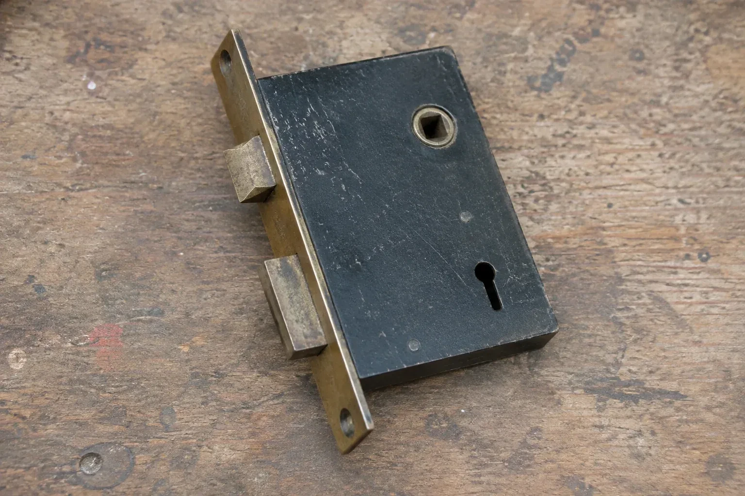 Closed mortise lock case with spindle opening, keyhole, latch and deadbolt on a wooden workbench. — Vintage Mortise Lock Service, Aurora